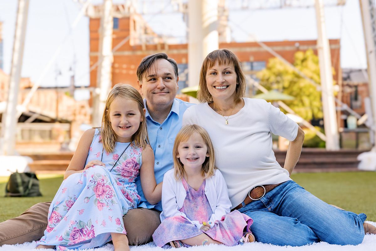 A family of four sitting on a blanket in front of the Lucky Strike tower at American Tobacco Campus in Durham, NC