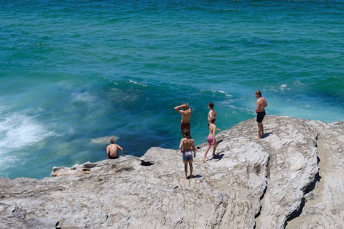 Group of teenage boys jumping off a rock into the ocean in Sydney, Australia
