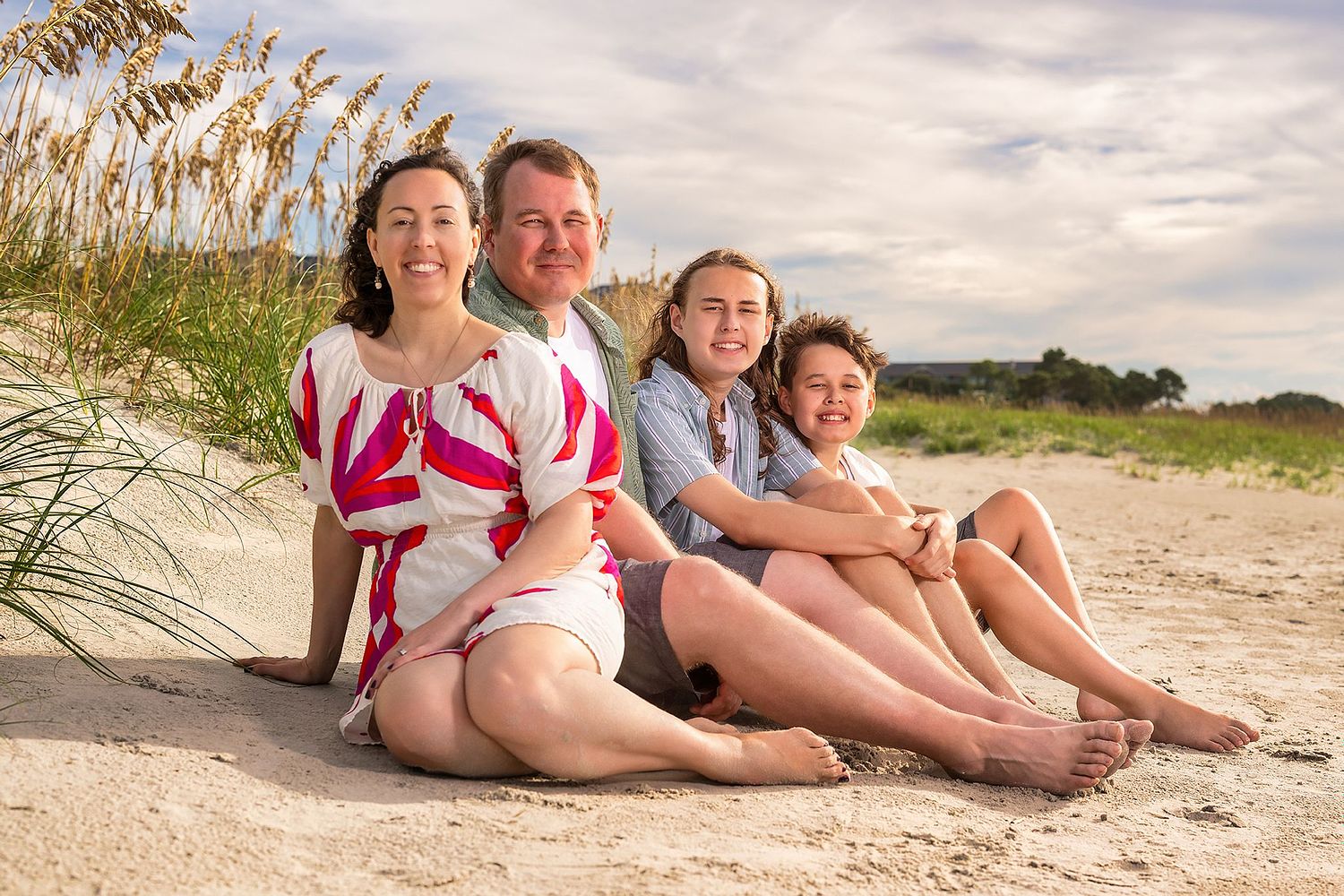 amily of four sitting on Hilton Head Island beach with beach grass in the background at sunrise during a professional family photography session.