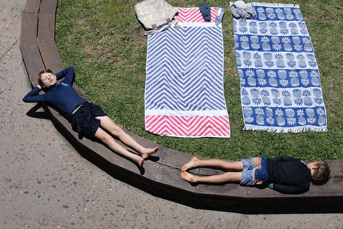 Two boys basking in the sun on the wood ledge instead of their beach towels