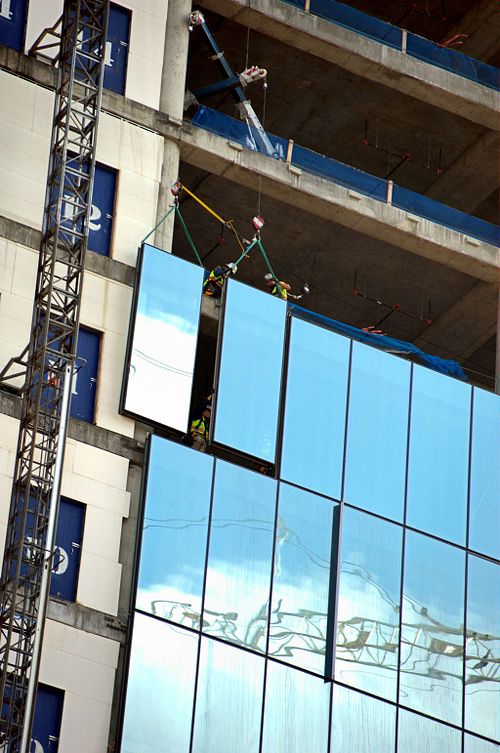 Workers install large glass panels on a skyscraper.