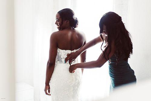 "damigella che allaccia vestito alla sposa di spalle"